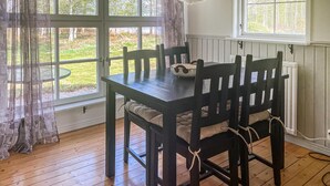 Una mesa de comedor con sillas, una ventana con cortinas y vistas al exterior con vegetación.