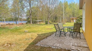 Un patio con mesa y sillas, un cobertizo pequeño y vistas a un lago y árboles.