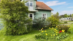 Une maison à deux étages dotée d’un balcon, entourée de verdure et de fleurs.