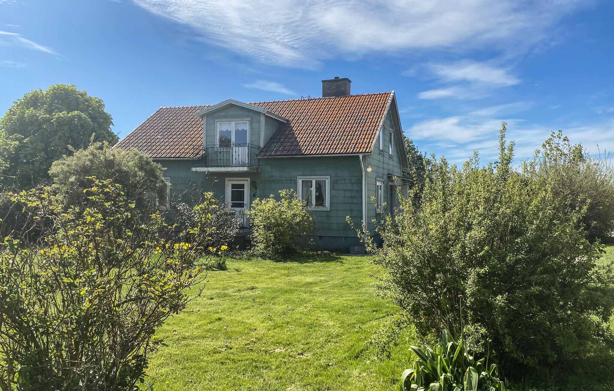 A two-story house with a red-tiled roof, surrounded by greenery and a well-maintained lawn.