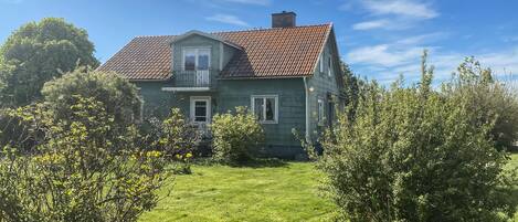 A two-story house with a red-tiled roof, surrounded by greenery and a well-maintained lawn.