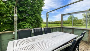 Une terrasse extérieure avec une table et des chaises en bois, une lanterne suspendue et une vue sur un paysage verdoyant.
