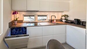 Cozinha compacta com armários brancos, forno embutido, pia e janela sobre o balcão.
