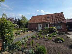 A brick house with a tiled roof, a garden with various plants and rocks, and a paved pathway.