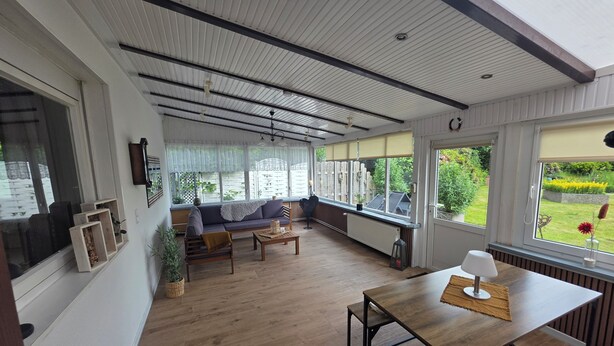 Ein Zimmer mit einer Couch, einem Tisch und großen Fenstern mit Blick auf den Garten.