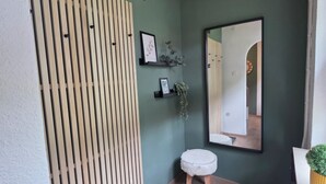 Ein Zimmer mit einer Holztrennwand, einem kleinen Hocker, einem Spiegel und einem Blumentopf.