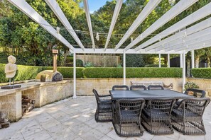 Eine Außenpatio mit einer Pergola, einer Steinmauer und einem Tisch mit Korbstühlen.