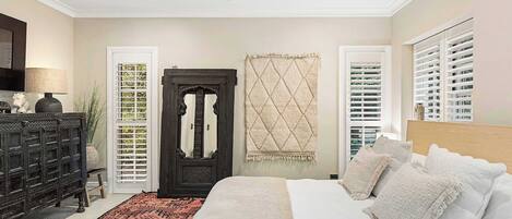 A bedroom with a bed, a ceiling fan, a dark wooden dresser, a patterned rug, and a decorative door.