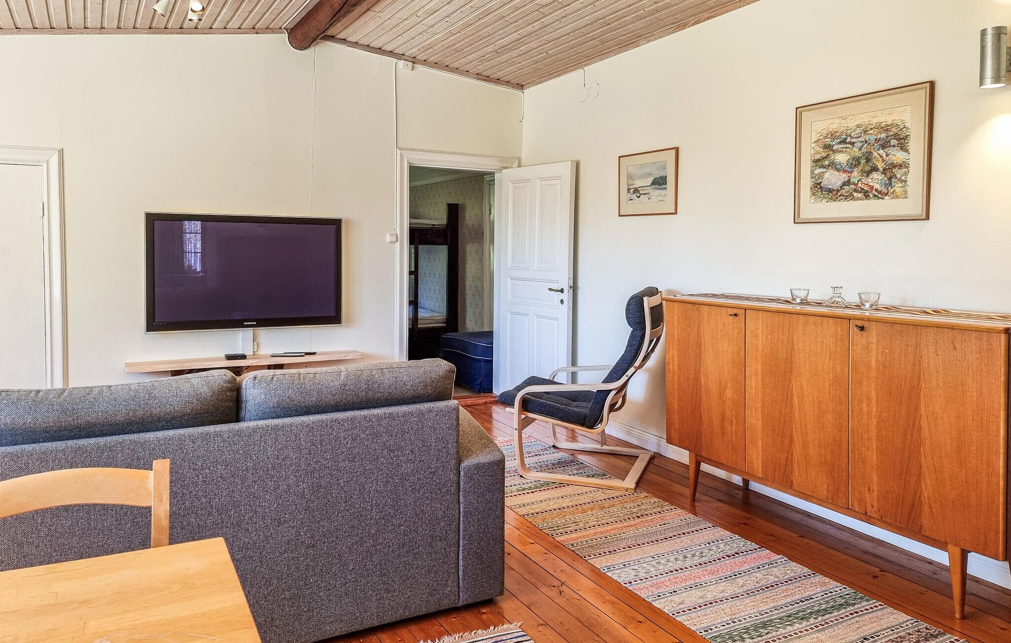 A living room with a flat-screen TV, grey sofas, a wooden cabinet, and a patterned rug.