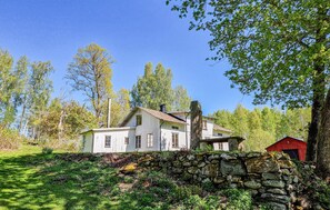 Ett lantligt hus med en stenmur och en röd ladugård, beläget i ett skogsområde.