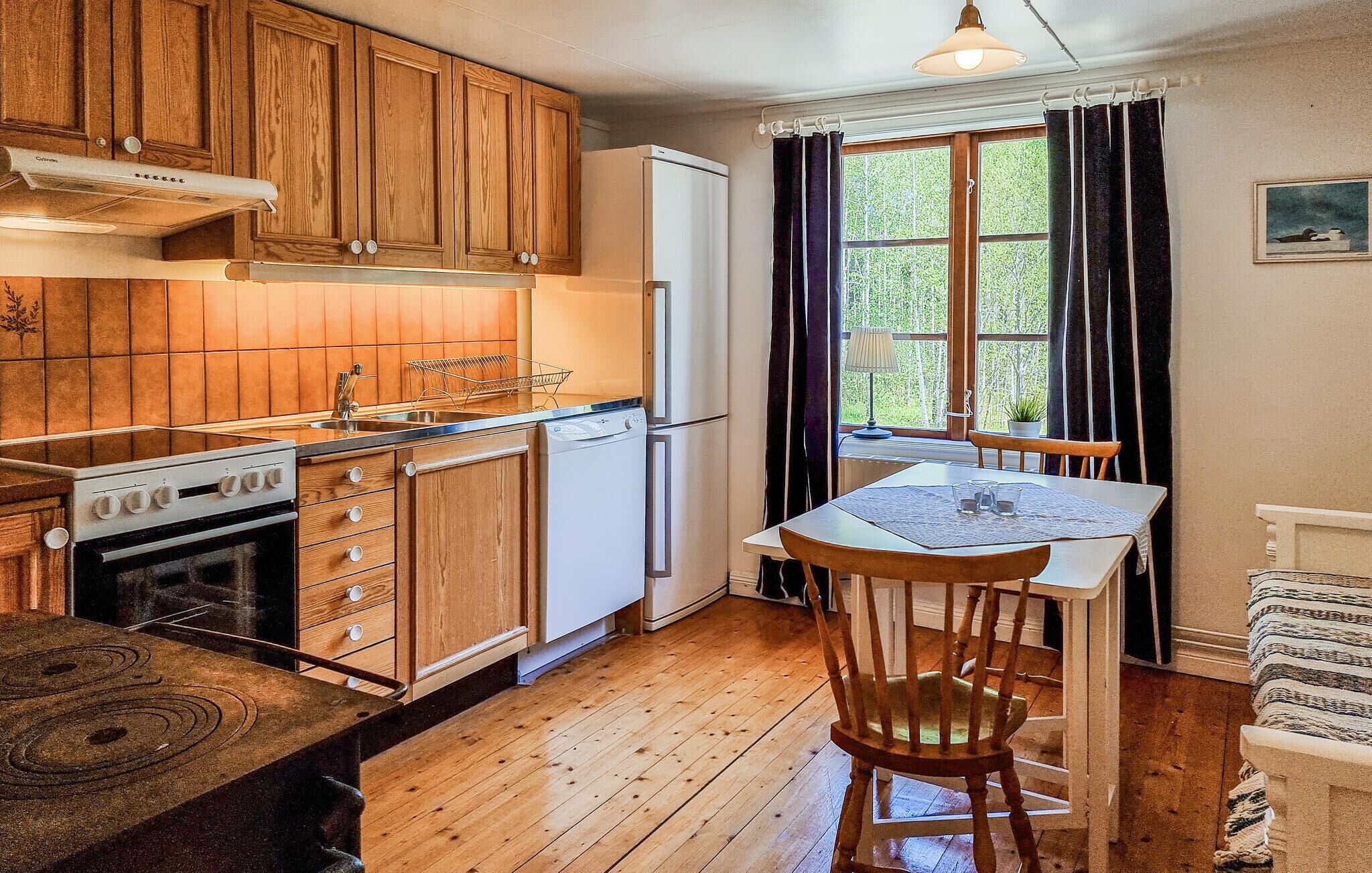 A compact kitchen with wooden cabinets, a white refrigerator, a stove, and a dining area with a table and chairs.