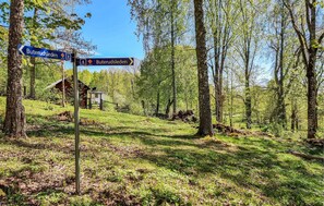 En vägskylt med anvisningar till vandringsleden Buterudsleden, omgiven av ett skogsområde med en liten byggnad i bakgrunden.