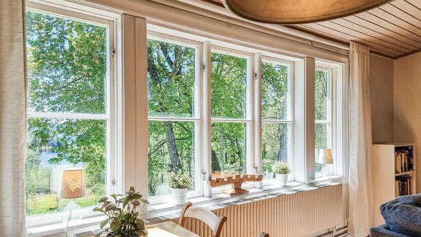 A room with large windows, a radiator, a table, chairs, and a bookshelf. - 3 bedroom lovely home in Håverud (Håverud)
