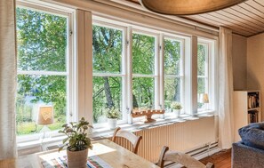 A room with large windows, a radiator, a table, chairs, and a bookshelf. - 3 bedroom lovely home in Håverud (Håverud)