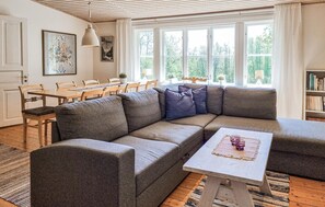 Ett modernt vardagsrum med en hörnsoffa, ett matbord och stora fönster.