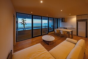 A modern living room with a large sliding glass door leading to a balcony with a view of the sea.