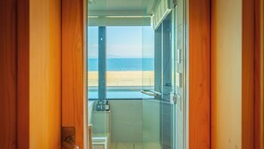 Une salle de bain dotée d’une porte en verre donnant sur un balcon avec vue sur la plage.