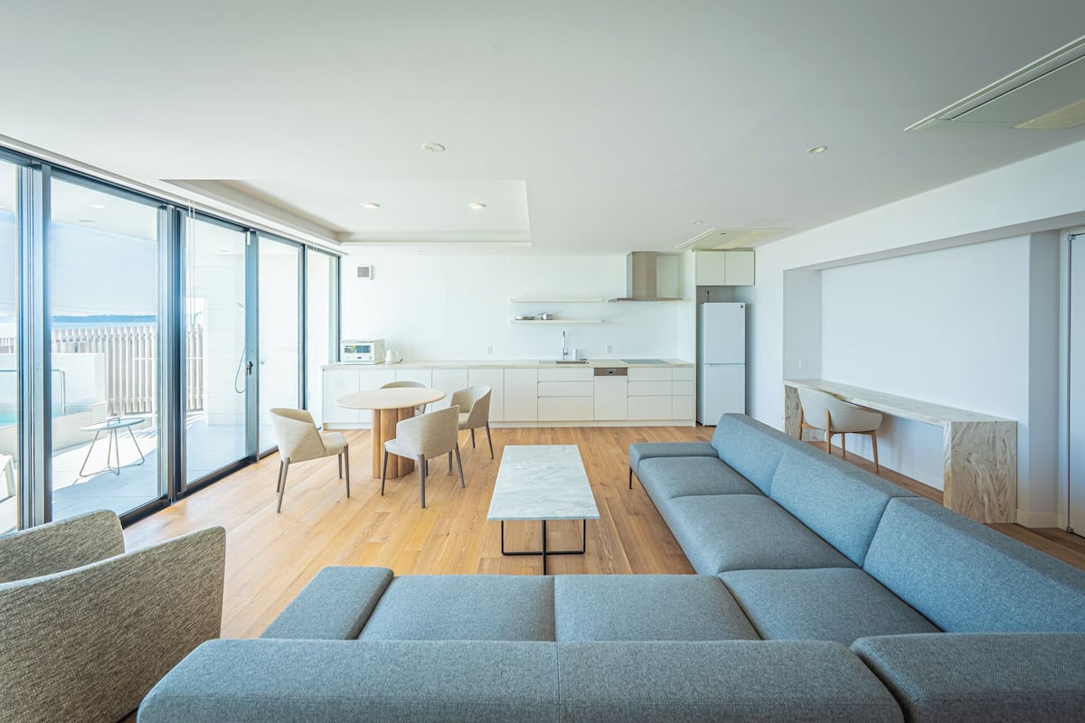 Una sala moderna con un sofá seccional gris grande, una mesa redonda de centro y una zona de comedor con una mesa redonda pequeña y sillas.