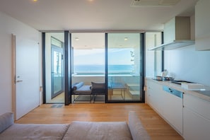 Una cocina moderna con vista al mar, un comedor con mesa y sillas, y un puerta corrediza de vidrio que da a un balcón.
