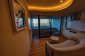 Un interior moderno con piso de madera, una zona de estar con una mesa redonda y vistas al mar a través de grandes puertas de vidrio.