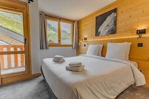 Ein Schlafzimmer mit Holz-Kopfteil, einem großen Fenster mit Bergblick und einem Bett mit weißen Bettwäsche und Handtüchern.