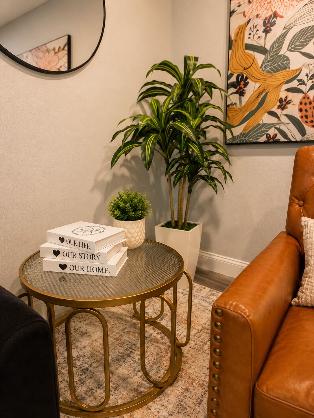 Une pièce avec une table ronde, une plante en pot, un canapé en cuir et une œuvre d’art encadrée au mur.