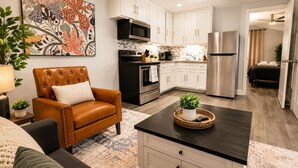 A modern kitchen with white cabinets, stainless steel appliances, and a dining area with a leather chair and a small table. - Cozy 1BR Near Med Center, NRG & Downtown (Houston)