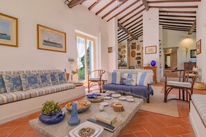 Ein gemütliches Wohnzimmer mit einer Couch, Sesseln, einem Couchtisch mit Dekoration und Blick auf den Garten durch eine Tür.