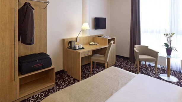 A hotel room with a bed, desk, chair, TV, and a wardrobe with hanging clothes. - 2 Person Holiday Park Home in Dortmund (Dortmund)
