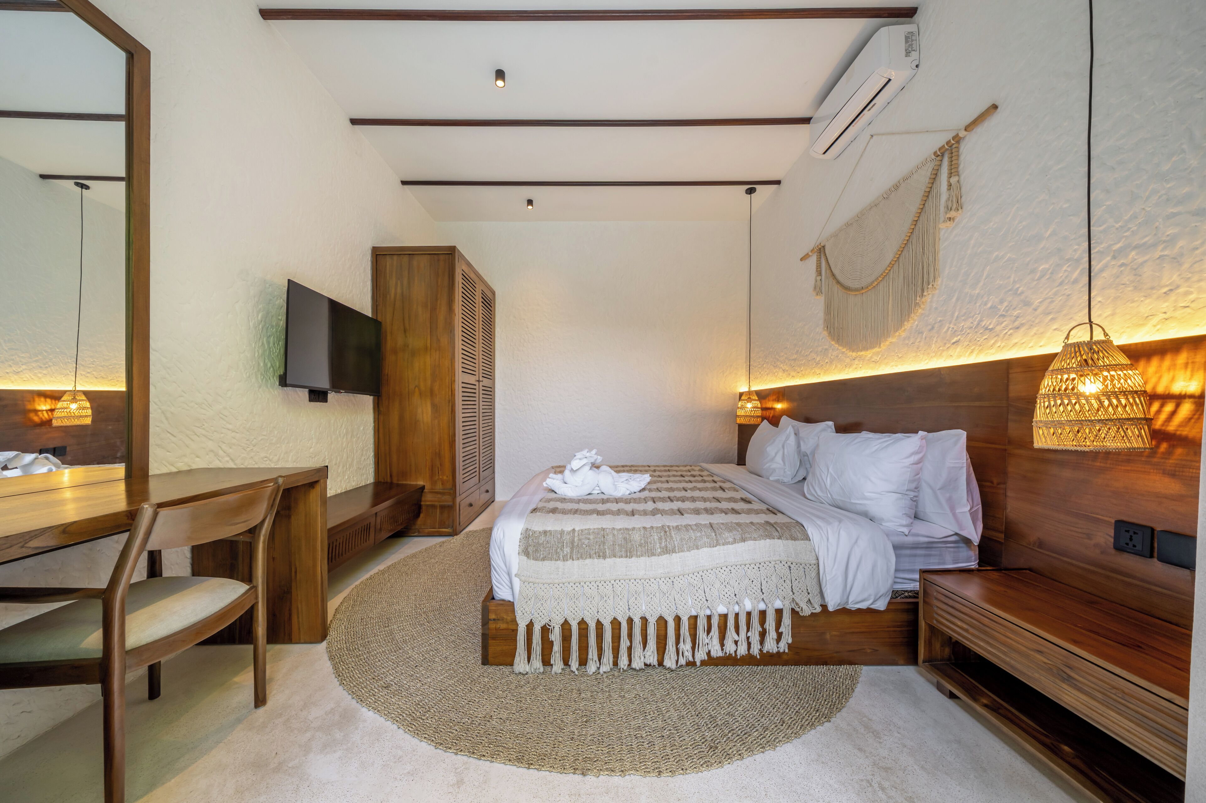 A bedroom with a bed, bedside table, chair, TV, and a wall-mounted air conditioner.
