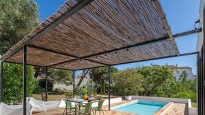 Ein überdachter Außenbereich mit Pool, einem Tisch mit Stühlen und einer Pergola.