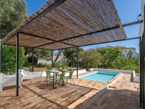 Ein überdachter Außenbereich mit Pool, einem Tisch mit Stühlen und einer Pergola.