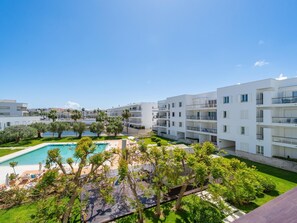 Ein moderner Apartmentkomplex mit Schwimmbad, üppiger Bepflanzung und blauem Himmel.