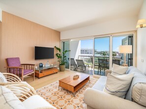 Ein modernes Wohnzimmer mit Flachbildfernseher, Holzpaneele, großen Schiebeglasüren zu einem Außenbalkon und einer Couch.