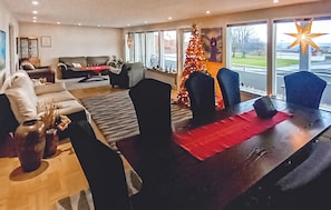 Uma sala de estar moderna com área de jantar, janelas amplas e um pinheiro de Natal.