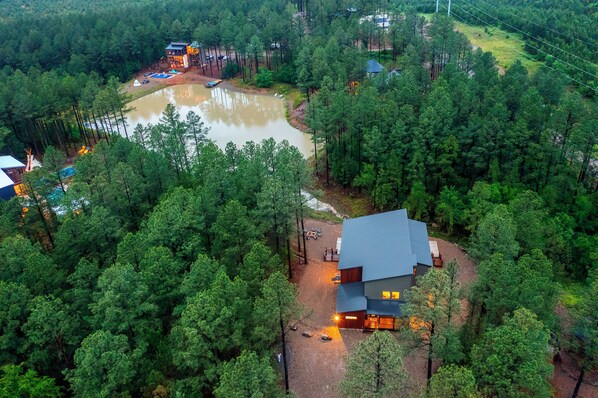 Eine Lodge, umgeben von dichtem Wald, einem Teich und einem klaren Himmel.