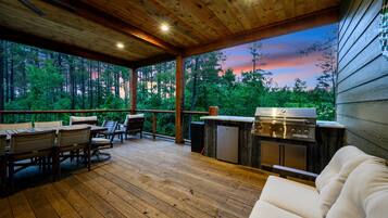 Une terrasse extérieure dotée d’un plafond en bois, d’un barbecue et d’un espace salon avec un canapé et des fauteuils.