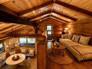 Ein gemütliches Blockhaus-Interieur mit Schlafzimmer im Zwischengeschoss, Essbereich und einer Sitzecke.