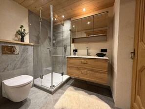 Ein modernes Badezimmer mit Duschkabine aus Glas, Toilette, Holzwaschtisch mit Spüle und Spiegel über dem Waschtisch.