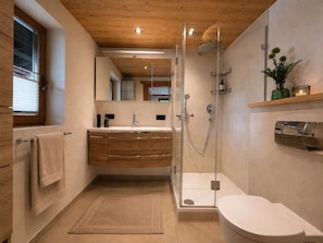 Ein modernes Badezimmer mit einer Duschkabine aus Glas, einem Holzwaschtisch, einem großen Spiegel und einer Toilette.