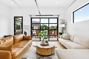 A modern living room with a large window, leather sofas, a round coffee table, and a view of the outdoors.