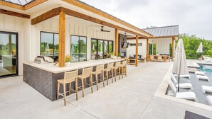 A covered outdoor bar area with a pool and lounge chairs.