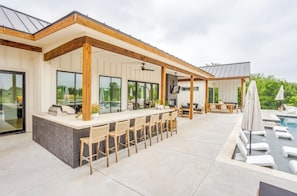 Ein überdachter Außenbereich mit Bar, Pool und Liegestühlen.