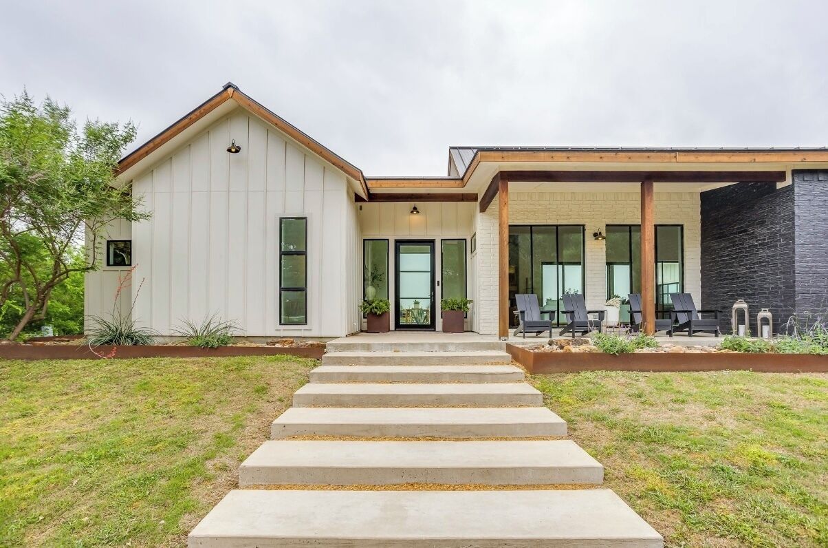 A modern two-story house with a front porch, large windows, and a stone exterior wall.