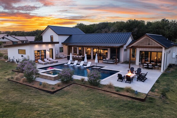 A modern house with a large outdoor pool, multiple seating areas, and a well-maintained lawn.