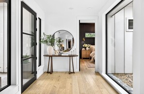 A hallway with a wooden floor, a round mirror on a table, and a view into a room with a sofa and a cabinet.