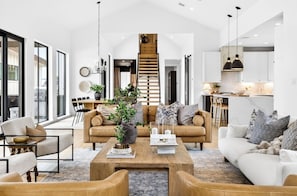 A modern living room with a central coffee table, sofas, and a staircase.