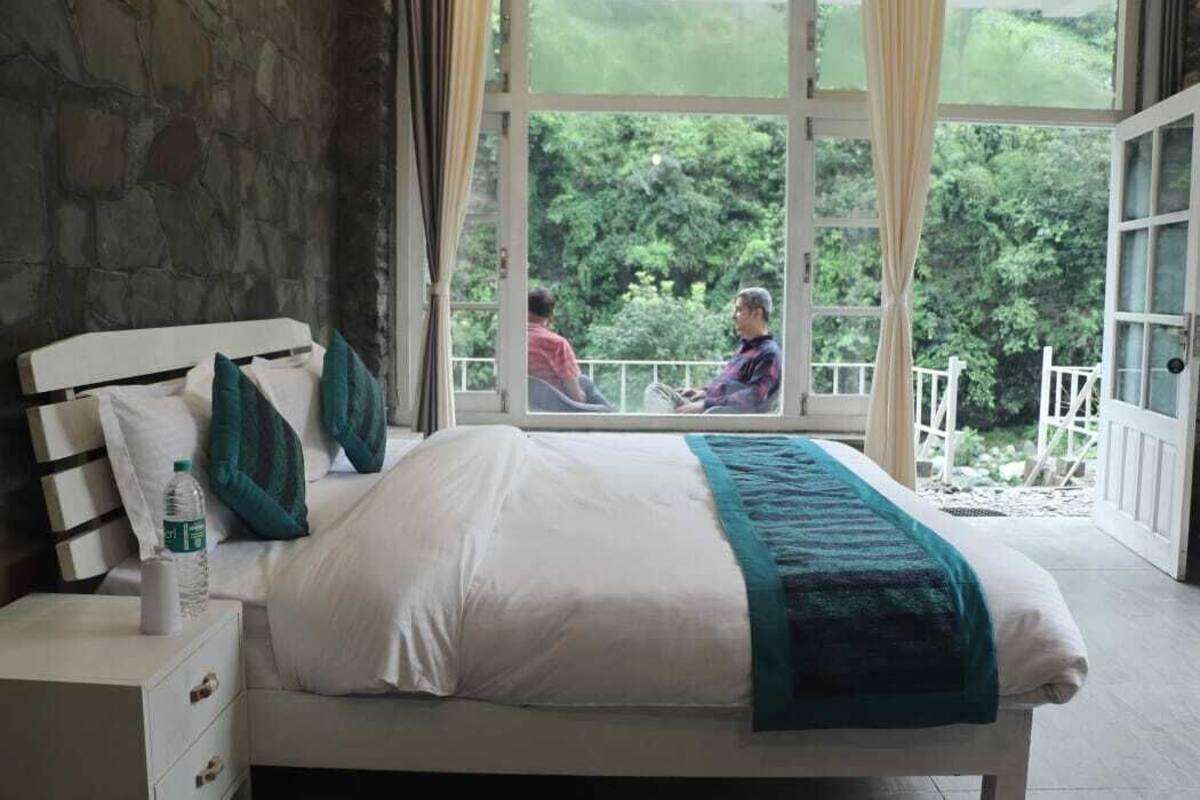 Un dormitorio con un ventanal grande, una cama, una mesita de noche y vistas a un balcón con gente en el exterior.