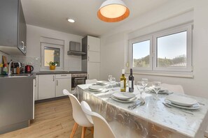 A modern kitchen with white cabinets, a marble countertop, and a dining area with a table set for two. - Holiday flat with full amenities (Štinjan)