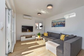 A modern living room with a grey sofa, a flat-screen TV, a small side table with a plant, and a painting on the wall. - Holiday flat with full amenities (Štinjan)